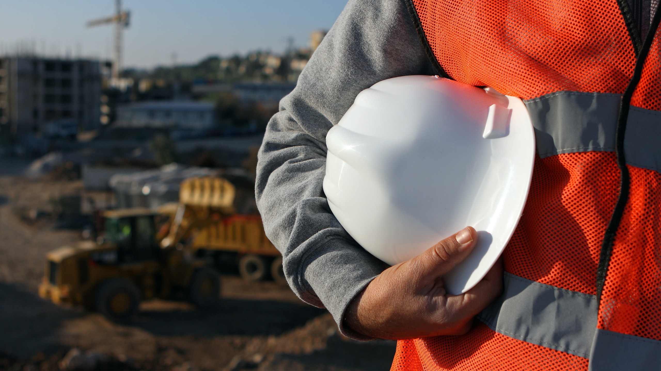 Construction worker in orange vest holding a white hard hat to his side under his arm