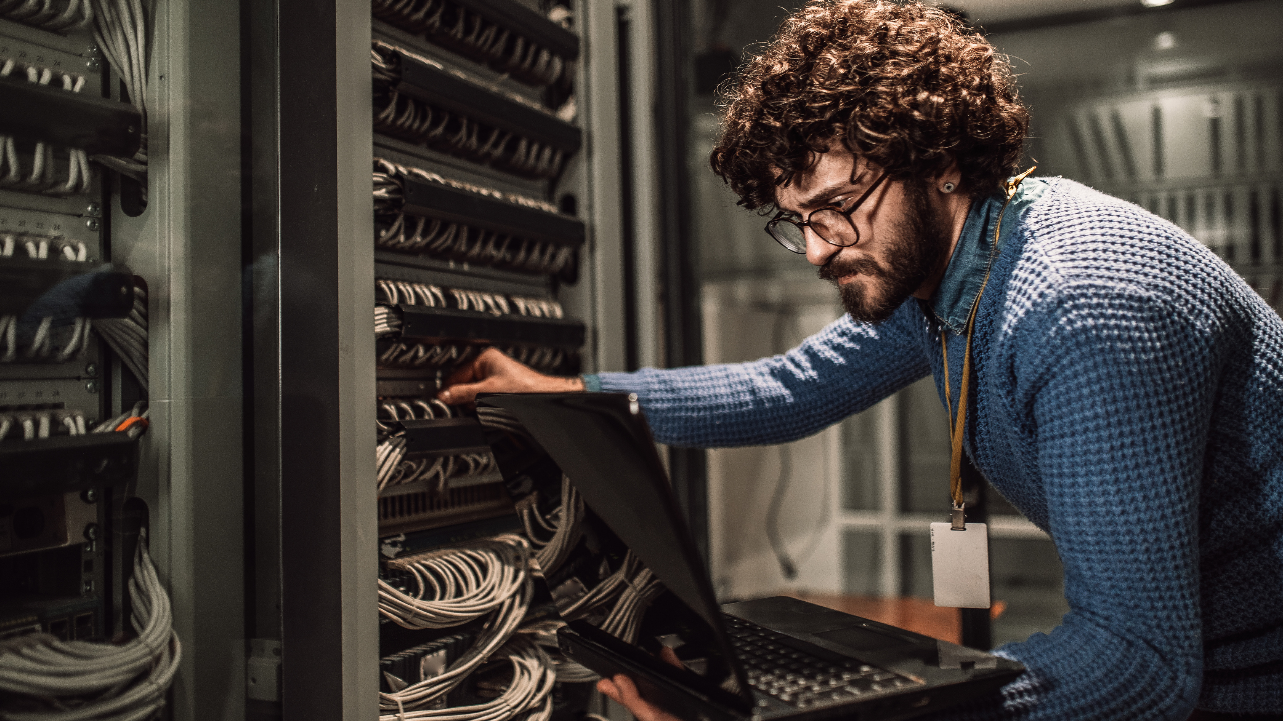 IT expert holding laptop and touching cords connected to a server
