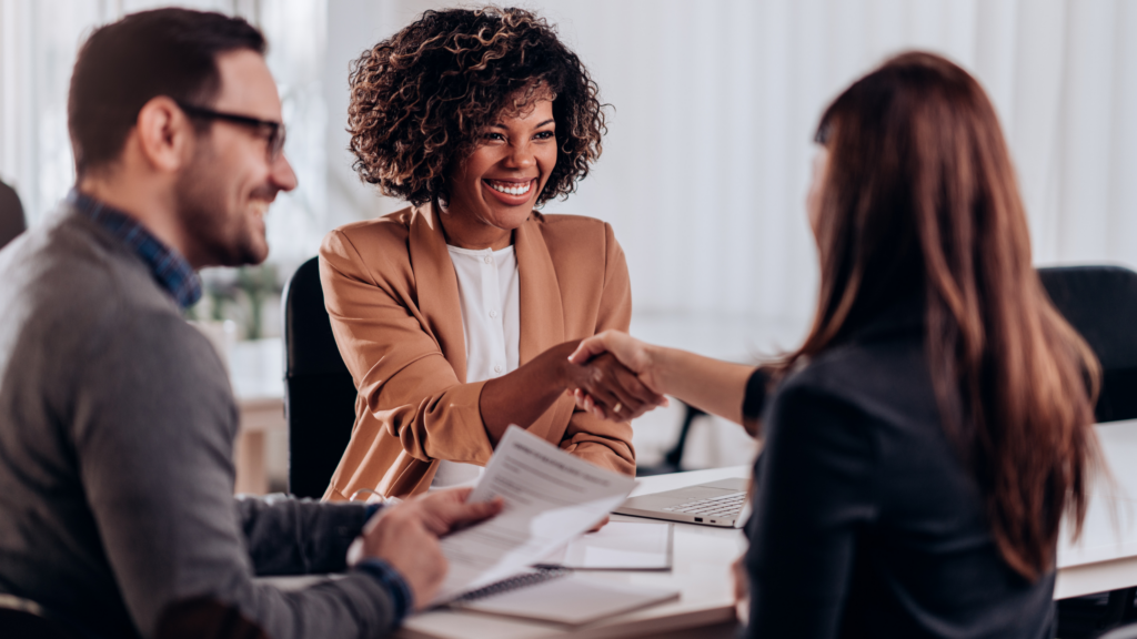 Woman shaking other woman's hand across a table to start behavioral interviewing process