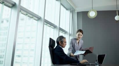 Interim executive assistant handing paper to executive at large desk in front of window