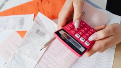 Hands typing on red calculator to determine cost of hiring temporary staff with agency markups vs internal hiring costs