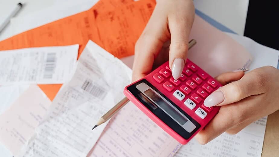 Hands typing on red calculator to determine cost of hiring temporary staff with agency markups vs internal hiring costs