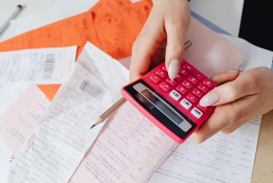 Hands typing on red calculator to determine cost of hiring temporary staff with agency markups vs internal hiring costs